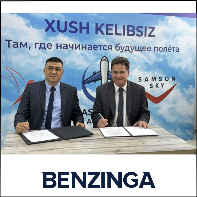 benzinga–leading-media-source-for-investors-2 Two men in suits sign documents at a table in front of a Samson Sky banner with aviation themes.