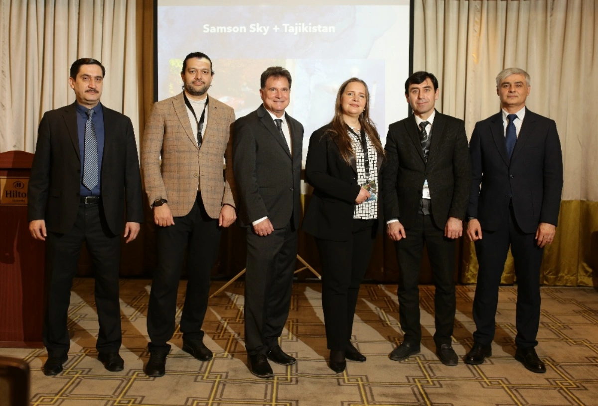 Samson Sky + Tajikistan group photo with six people standing in front of a projection screen at a Hilton hotel.