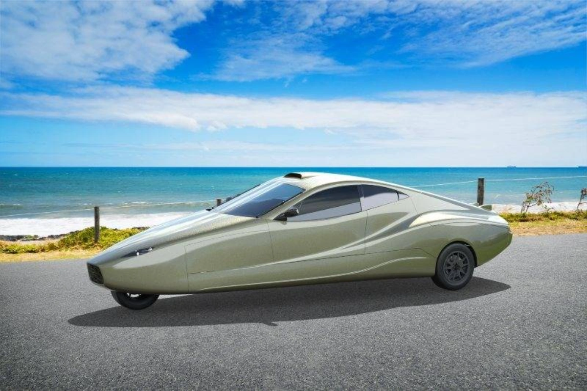 Sleek, futuristic, light gold three-wheeled car parked by the ocean on a sunny day.