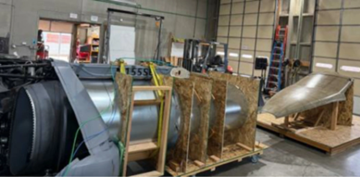 Industrial components in a workshop, including a large metal cylinder, and a curved panel on a wooden stand.