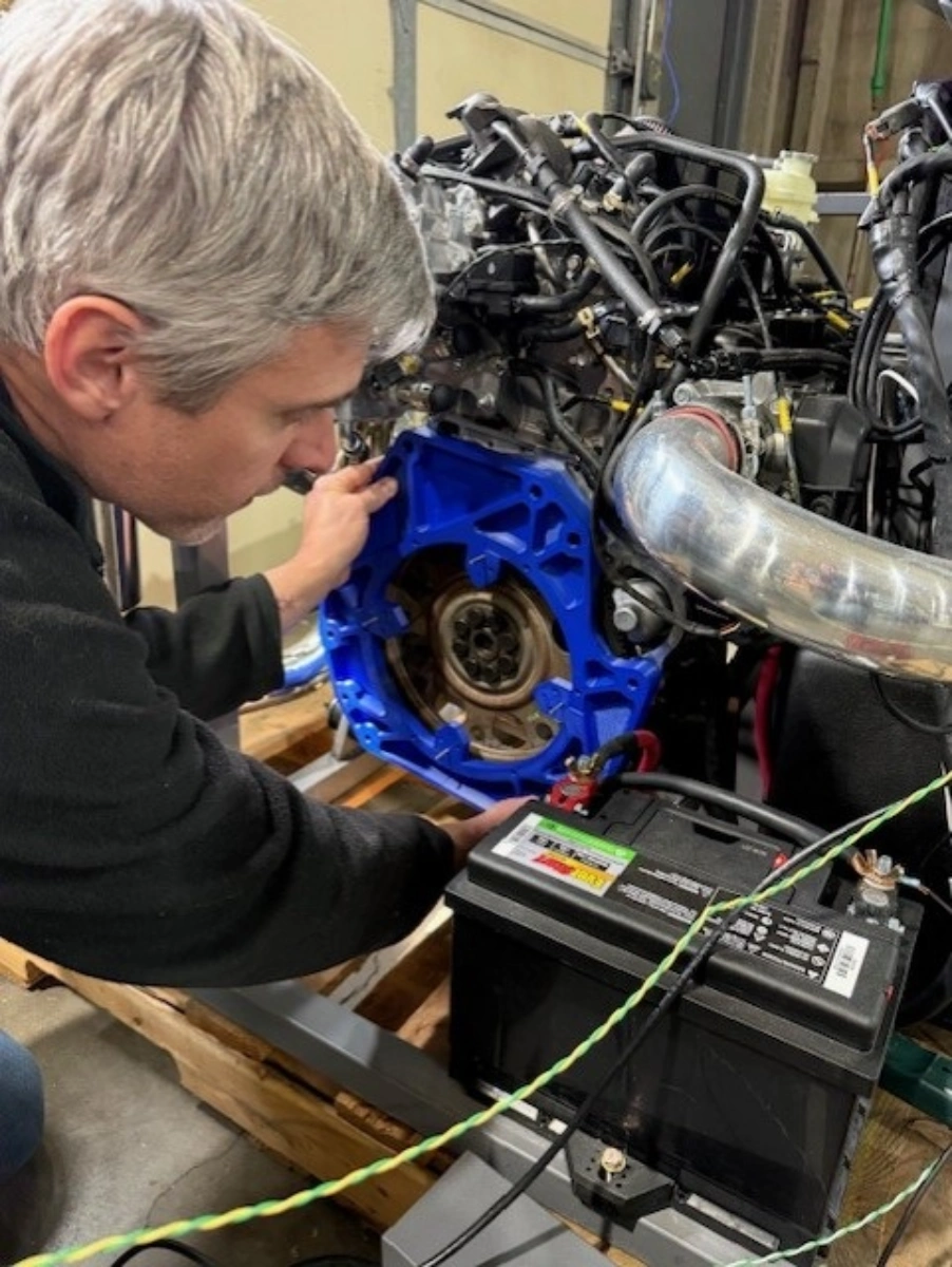 Mechanic inspecting a car engine on a test stand with a battery connected.