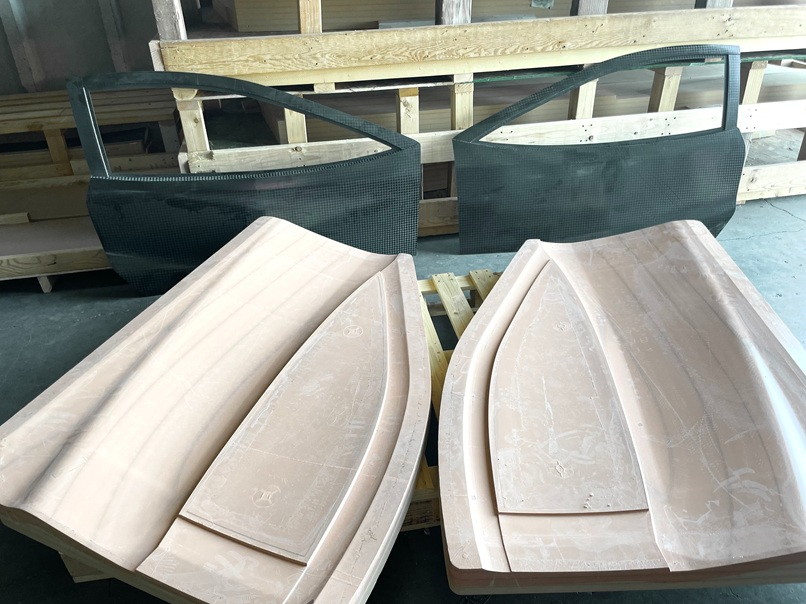 Two carbon fiber car doors and two wooden molds for car body panels.