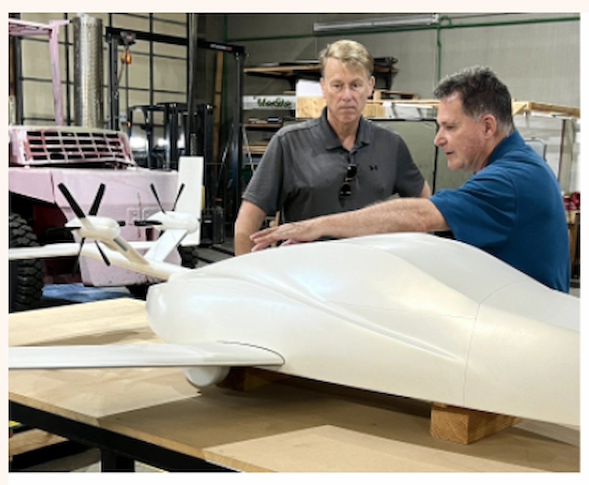Two men examine a white drone prototype with propellers in a workshop.